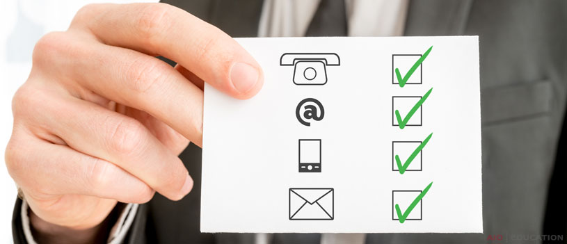 Osoba drží kartu s ikonami telefónu, e-mailu, mobilného telefónu a pošty, pričom každá je označená zelenou značkou začiarknutia, ktorá symbolizuje úspešnú komunikáciu. Je to rovnako efektívne ako vedieť ako napísať e-mail – jasné a profesionálne možnosti pripojenia na dosah ruky.