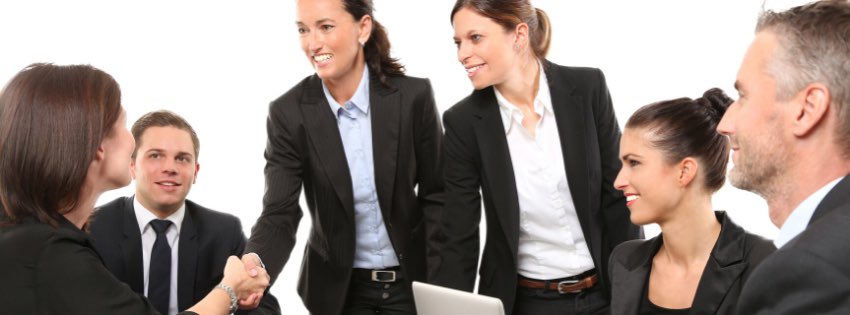 Skupina šiestich profesionálov v biznis oblečení, vrátane dvoch žien, ktoré si podávajú ruky, má stretnutie o výbere vhodných kandidátov. Všetci sa usmievajú, obklopení bielym pozadím, v popredí je viditeľný notebook.