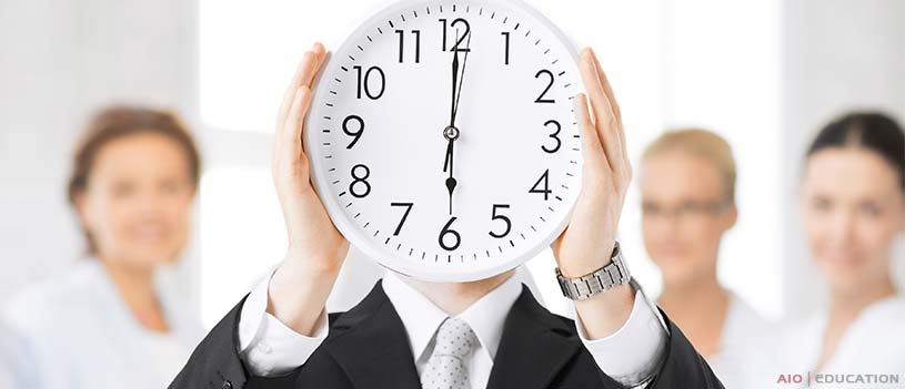 Človek v obleku drží pred tvárou veľké hodiny, ktoré symbolizujú podstatu riadenia času. Hodiny ukazujú 10:10, zatiaľ čo v pozadí zostávajú tri nevýrazné postavy, ktoré zdôrazňujú dôležitosť sebariadenia.