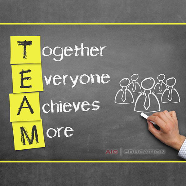 Ruka píše na tabuľu s lepiacimi papierikmi, ktoré hláskujú „TEAM“ zvisle, pričom zdôrazňujú motto: „Spoločne každý dosiahne viac.“ Kresby kriedou pri oslave leta na teambuildingu zobrazujú efektívne spolupracujúcich ľudí v oblekoch.